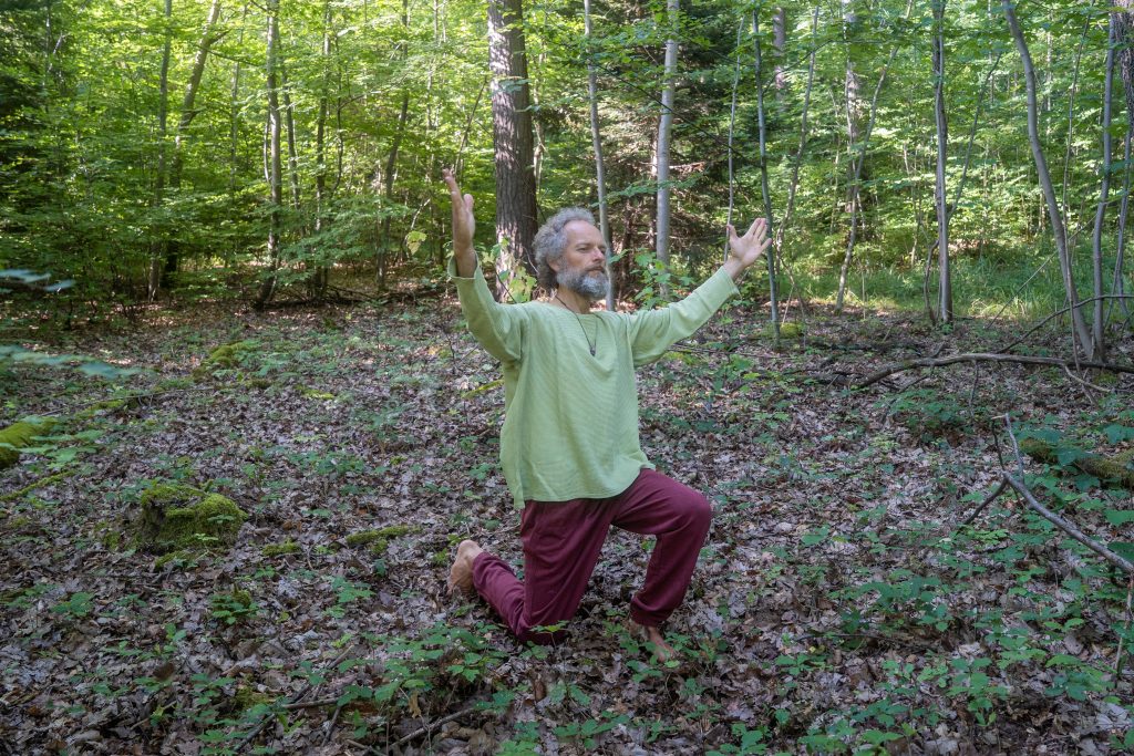 Alexander Hassenstein bei Körpermeditation aus dem Wyda im Wald. Knieend mit erhobenen armen.